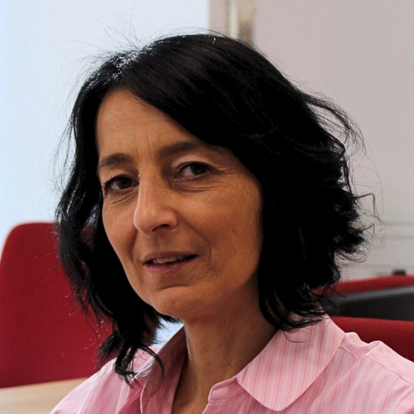 Cristina Pasere, voditeljica podrške operacijama usklađenosti u EOS Rumunjska, sjedi za svojim stolom u ružičastoj prugastoj bluzi i gleda u kameru.