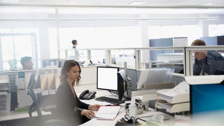 Digitalizacija: Tri zaposlenika su u uredu otvorenog tipa, žena sjedi među papirima ispred svog računala