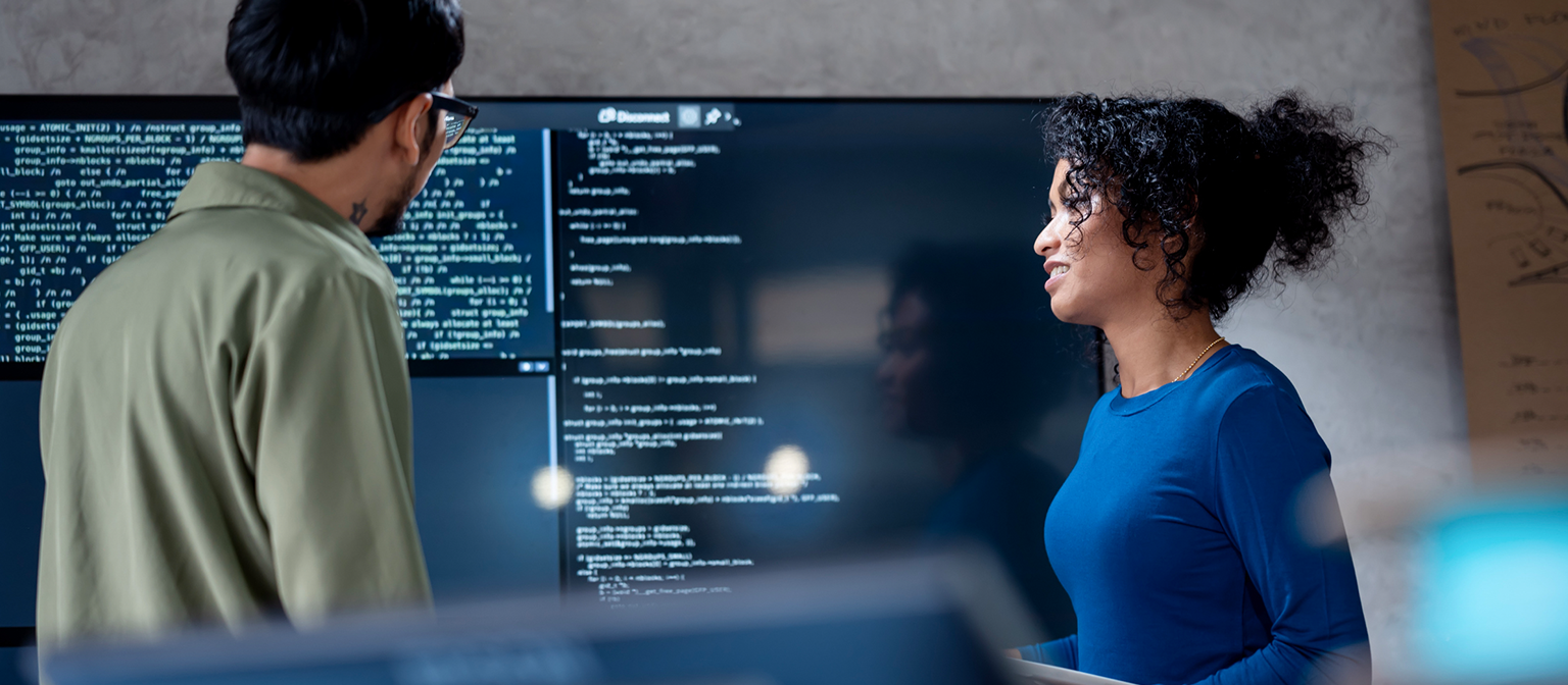 AI u naplati dugova: Na ovoj slici, dva stručnjaka zajednički analiziraju programski kod za automatizovane procese na velikom ekranu. Scena ilustruje praktičnu primenu veštačke inteligencije (AI) i robotizovane automatizacije procesa (RPA) u upravljanju dugovima — primer digitalne transformacije u upravljanju potraživanjima.