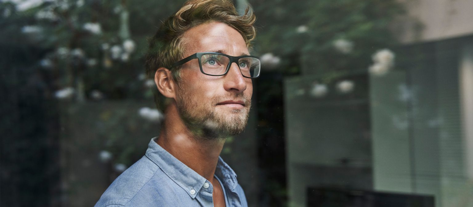 Mladi muškarac generacije Z zabrinuto gleda kroz prozor.